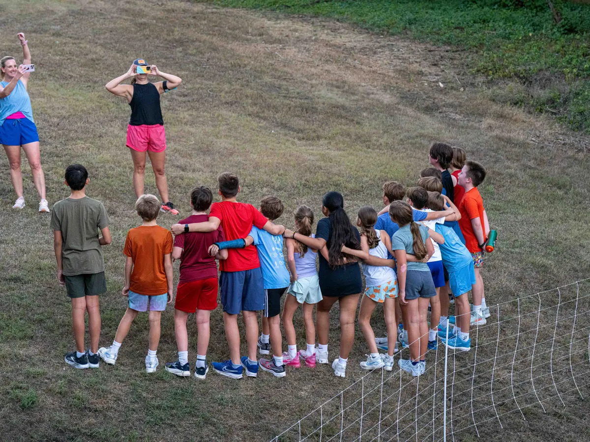 A group of children with arms around each other posing for photos on a grassy slope near the flock